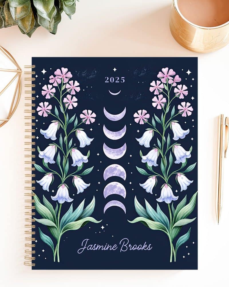 2025 spiral-bound planner with a dark blue cover featuring symmetrical floral designs and phases of the moon, personalized with the name Jasmine Brooks.