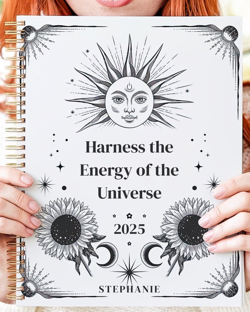 Hands hold a 2025 planner featuring a celestial sun design and the words Harness the Energy of the Universe.