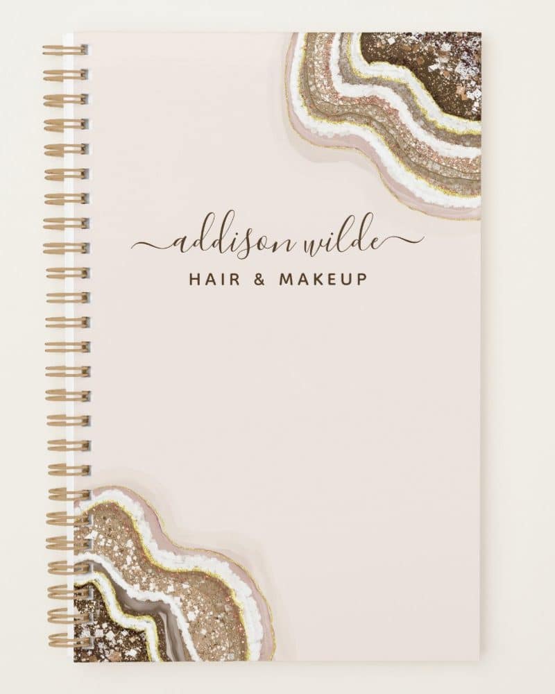 Spiral-bound notebook with a blush pink cover featuring gold and brown agate designs and the name Addison Wilde Hair & Makeup.