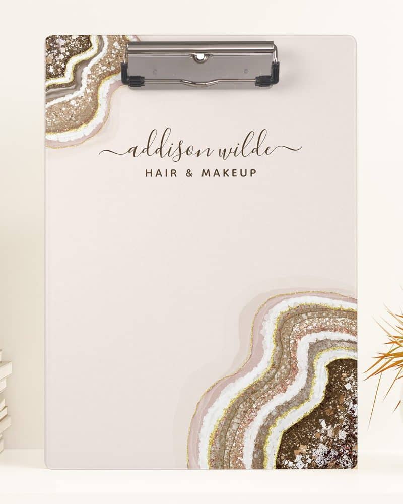 A clipboard with a blush pink background features an agate design and the name Addison Wilde Hair & Makeup.