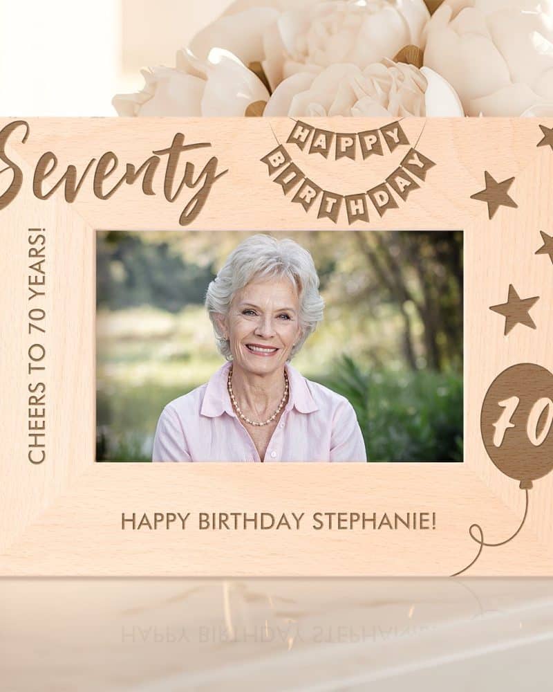 Wooden photo frame celebrating a woman's 70th birthday. The frame is engraved with "Seventy," "Happy Birthday," and "Cheers to 70 Years!" A photo of Stephanie is in the frame.