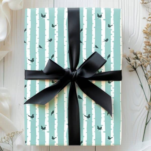 A Gift Wrapped In Light Teal Paper With A Pattern Of Birds On Birch Trees, Tied With A Black Ribbon.