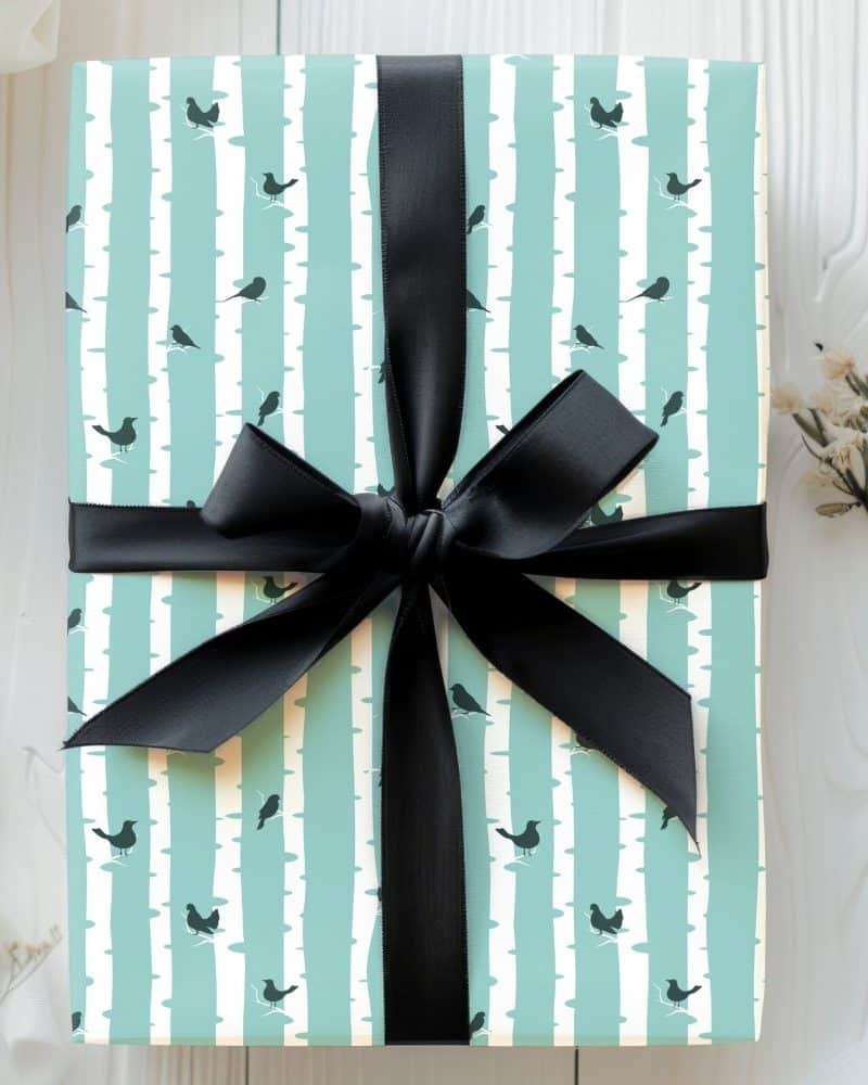 A gift wrapped in light teal paper with a pattern of birds on birch trees, tied with a black ribbon.