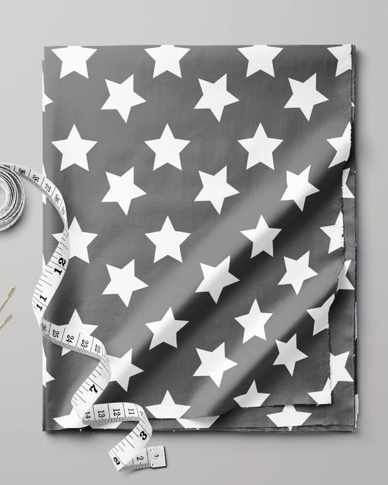 Grey fabric with a white star pattern, accompanied by a tape measure and needles.