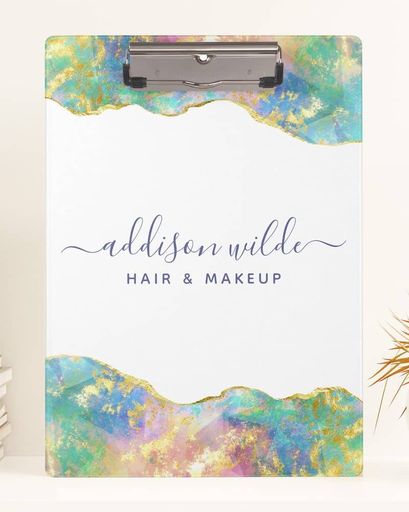 A clipboard with a pastel and gold abstract design and the text Addison Wilde Hair & Makeup.