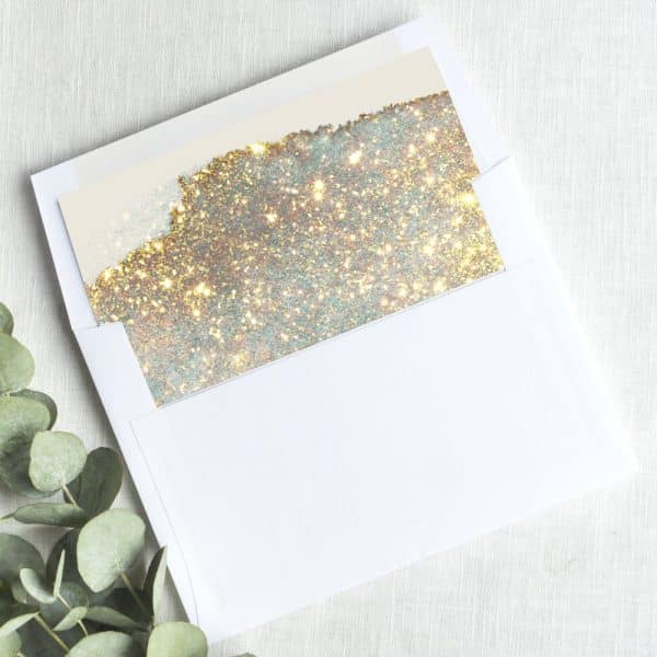 A White Envelope Containing A Gold And Silver Glitter Insert.