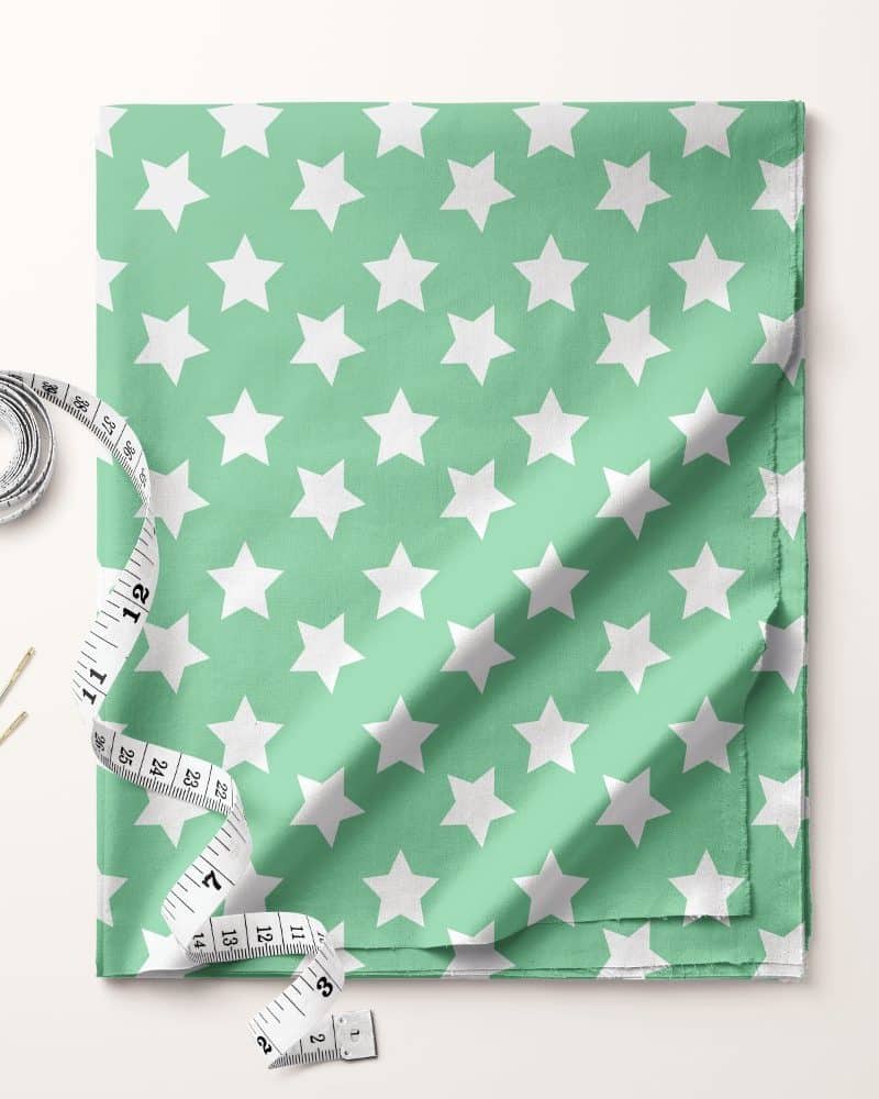 Light green fabric with a white star pattern, accompanied by a tape measure and needles.