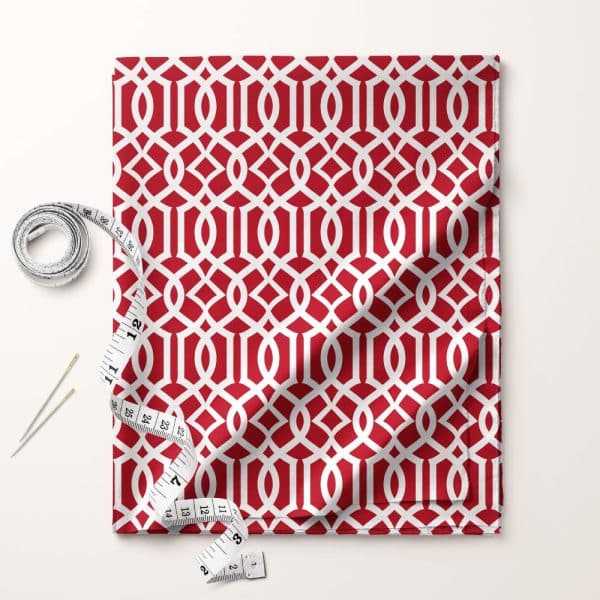 Red Fabric With A White Geometric Pattern, Partially Draped, Accompanied By A Tape Measure And Needles.