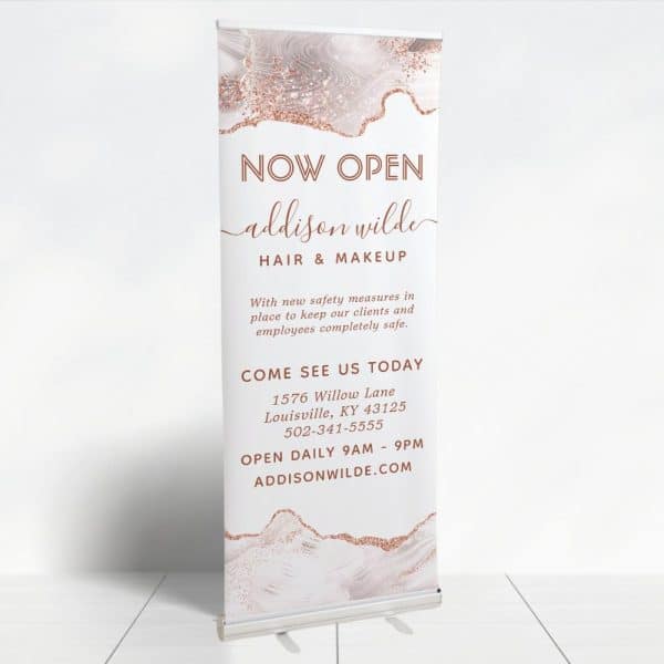 A Retractable Banner Announcing The Grand Opening Of Addison Wilde Hair &Amp; Makeup. The Banner Features A Rose Gold And White Marble Design.