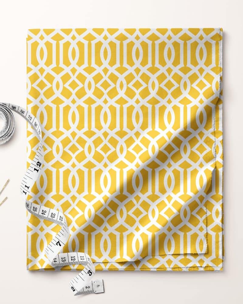 Mustard yellow fabric with a white geometric pattern, accompanied by a measuring tape and needles.