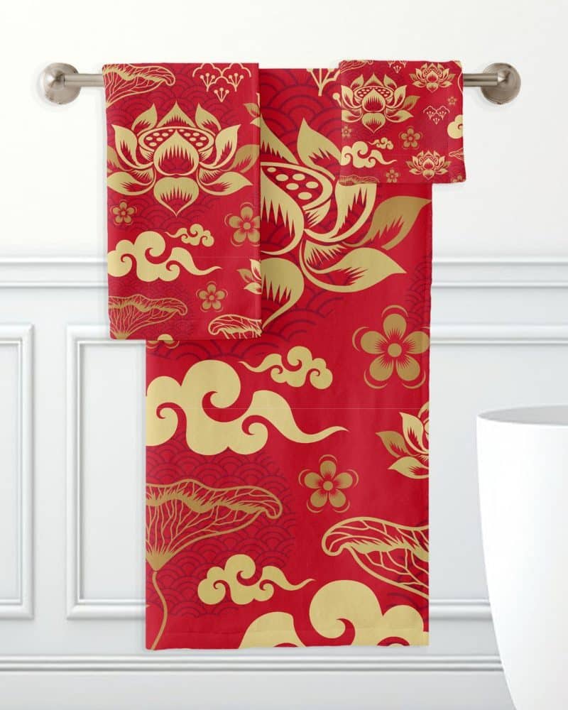 Red bath towels with a gold lotus flower and cloud pattern hanging on a towel rack.
