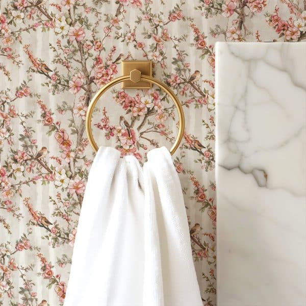 White Towel Hanging On A Gold Towel Ring Against A Floral Wallpaper.
