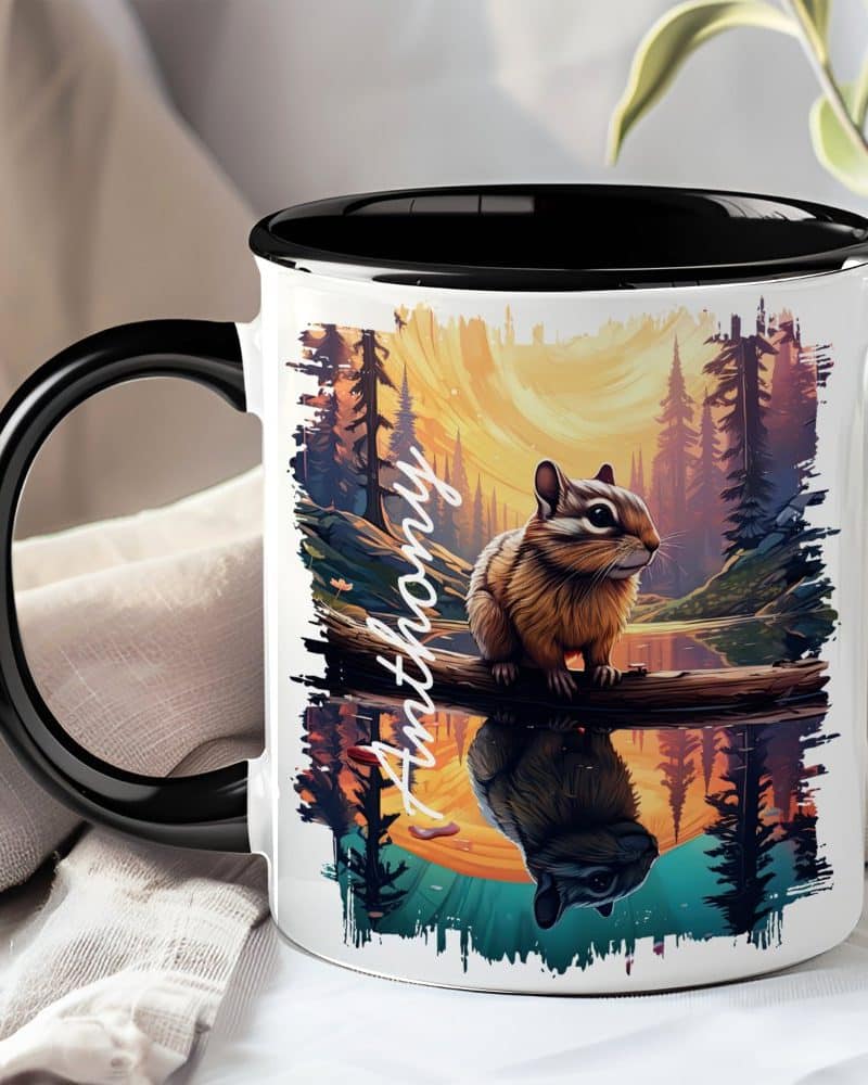 A coffee mug with a black handle and interior features a personalized name, Anthony, and an illustration of a chipmunk sitting on a branch over a reflective body of water at sunset.