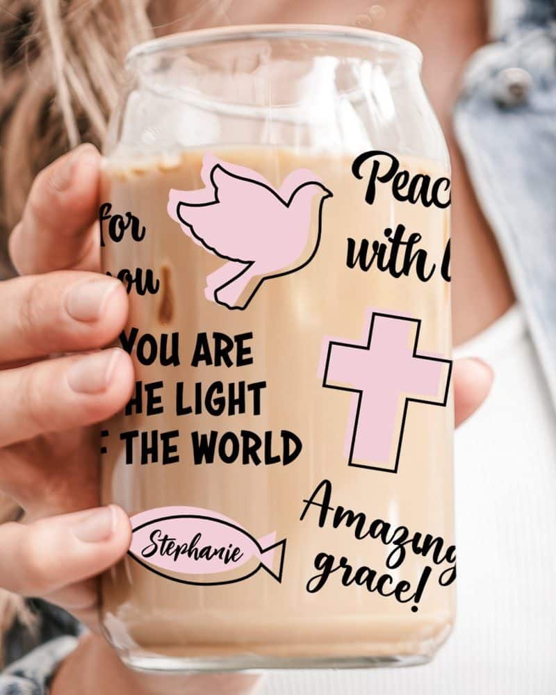 A person holds a glass iced coffee tumbler with religious-themed graphics and the name Stephanie.
