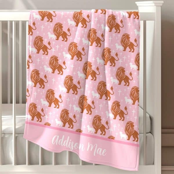Pink Baby Blanket With A Repeating Pattern Of Orange Lions And White Lambs, And Crosses. The Name Addison Mae Is Embroidered At The Bottom.