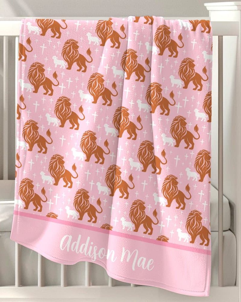 Pink baby blanket with a repeating pattern of orange lions and white lambs, and crosses. The name Addison Mae is embroidered at the bottom.