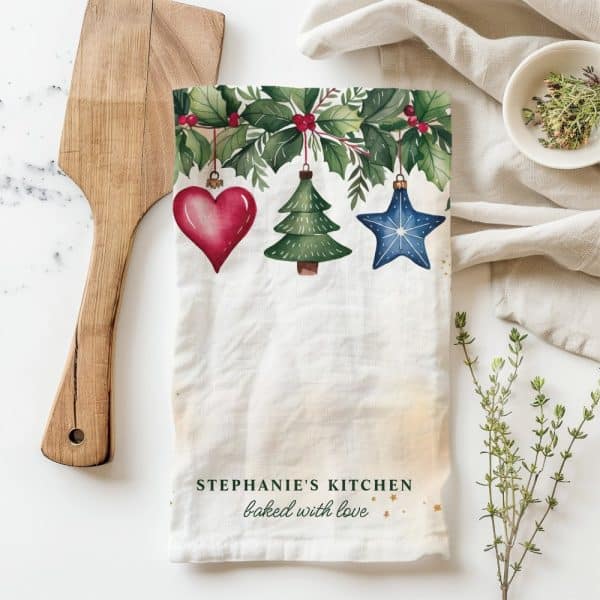 Christmas Tea Towel With A Holly Border And Hanging Ornaments: A Heart, Tree, And Star. The Text, Stephanie'S Kitchen, Baked With Love, Is At The Bottom.