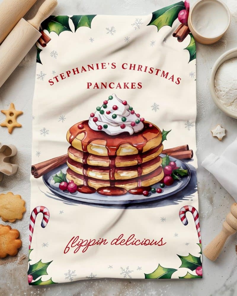 Christmas-themed tea towel featuring a watercolor illustration of a stack of pancakes topped with whipped cream and syrup.