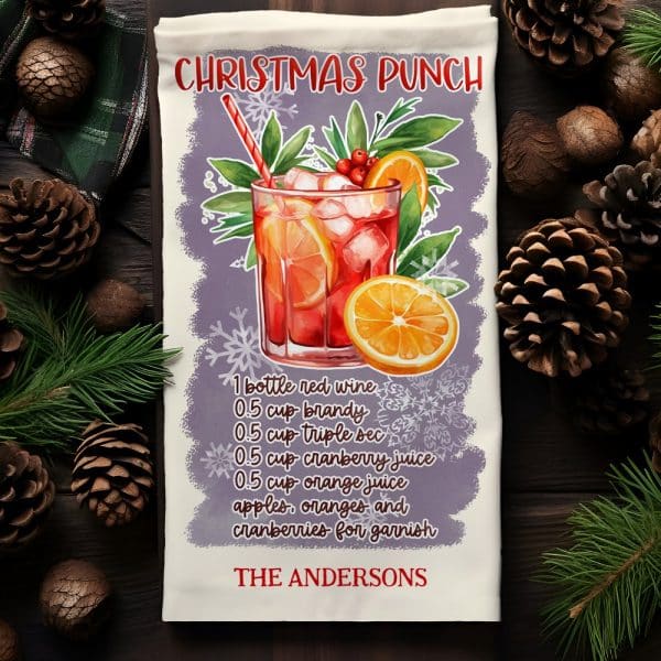 Christmas Punch Recipe On A Kitchen Towel, Showing A Glass Of The Punch Garnished With Fruit.
