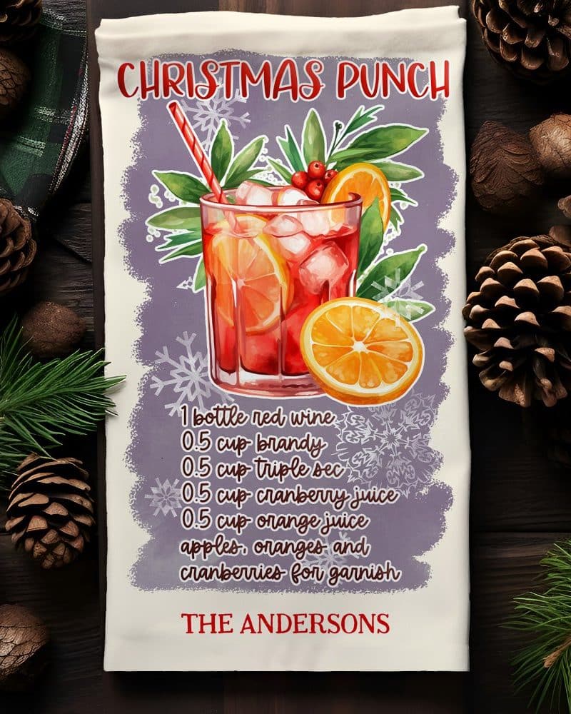 Christmas punch recipe on a kitchen towel, showing a glass of the punch garnished with fruit.