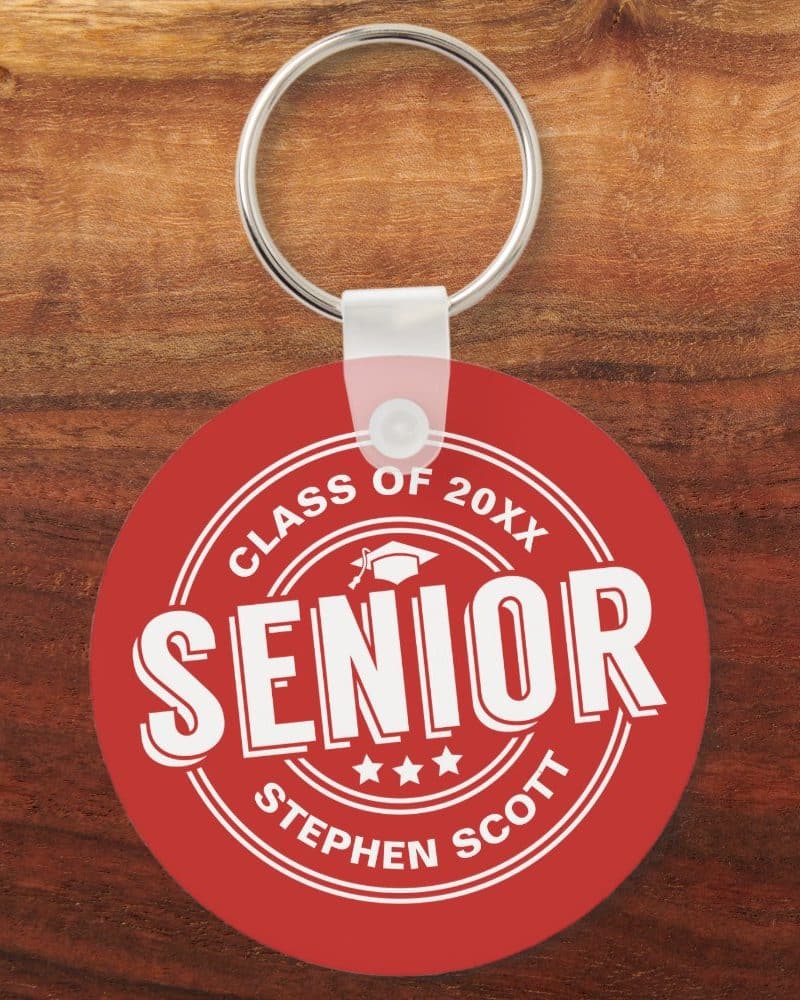 Red round keychain with white text. The text says Senior, Class of 20XX, and Stephen Scott. A graduation cap icon is also present.
