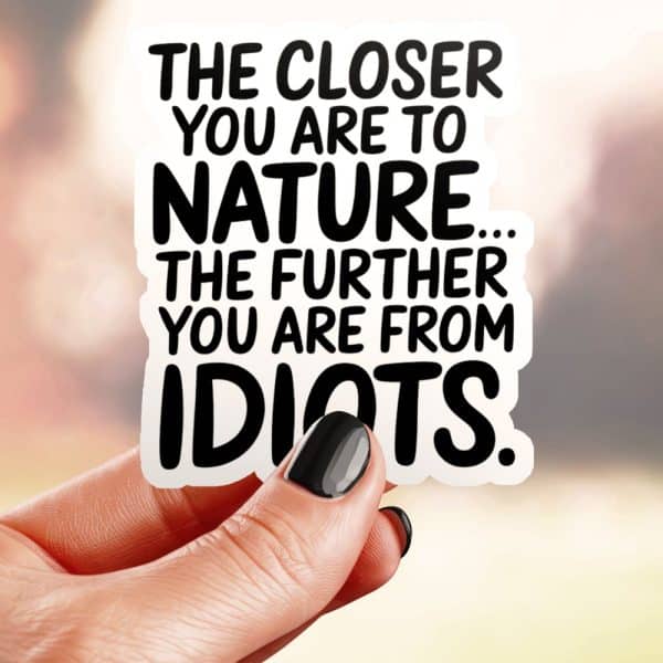 Hand Holding A Sticker That Reads: The Closer You Are To Nature, The Further You Are From Idiots.