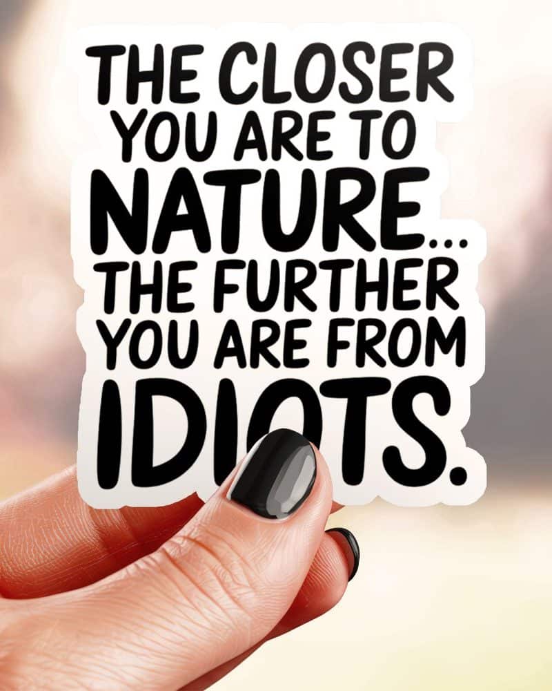 Hand holding a sticker that reads: The closer you are to nature, the further you are from idiots.