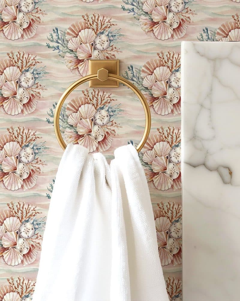 White towel hanging on a gold ring against a seashell patterned wallpaper.