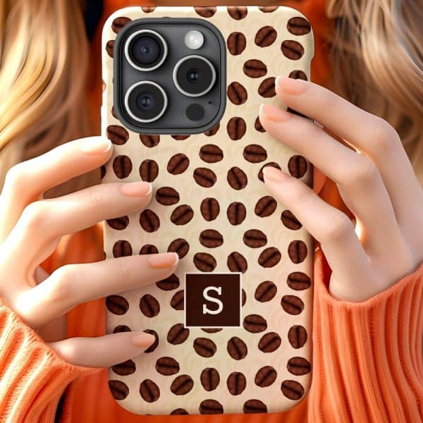 A Person Holds Up A Beige Iphone Case Covered In A Repeating Pattern Of Coffee Beans And A Brown Square With A White Letter S.