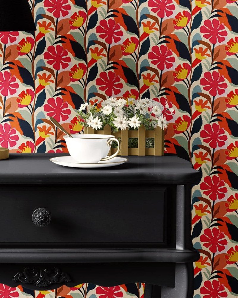 Black nightstand with a teacup and saucer, in front of a bold floral wallpaper.