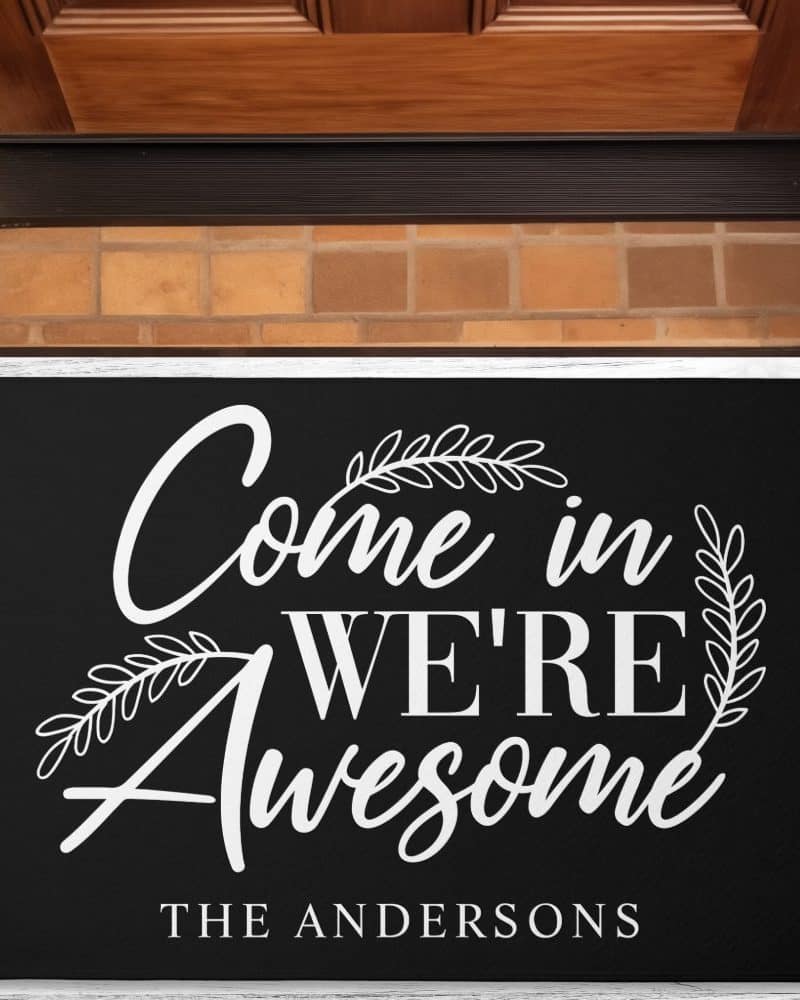 Black welcome mat with white lettering that says Come in We're Awesome, and The Andersons at the bottom.