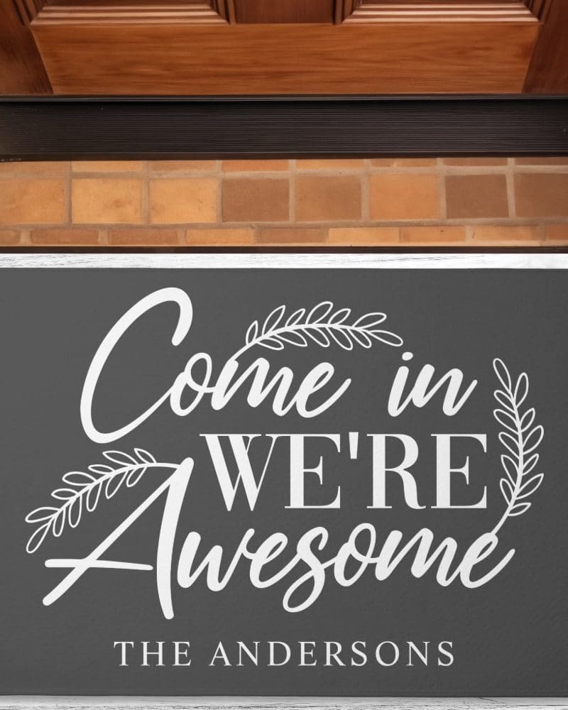 Dark gray doormat with white lettering that says Come in We're Awesome, and the name The Andersons below.