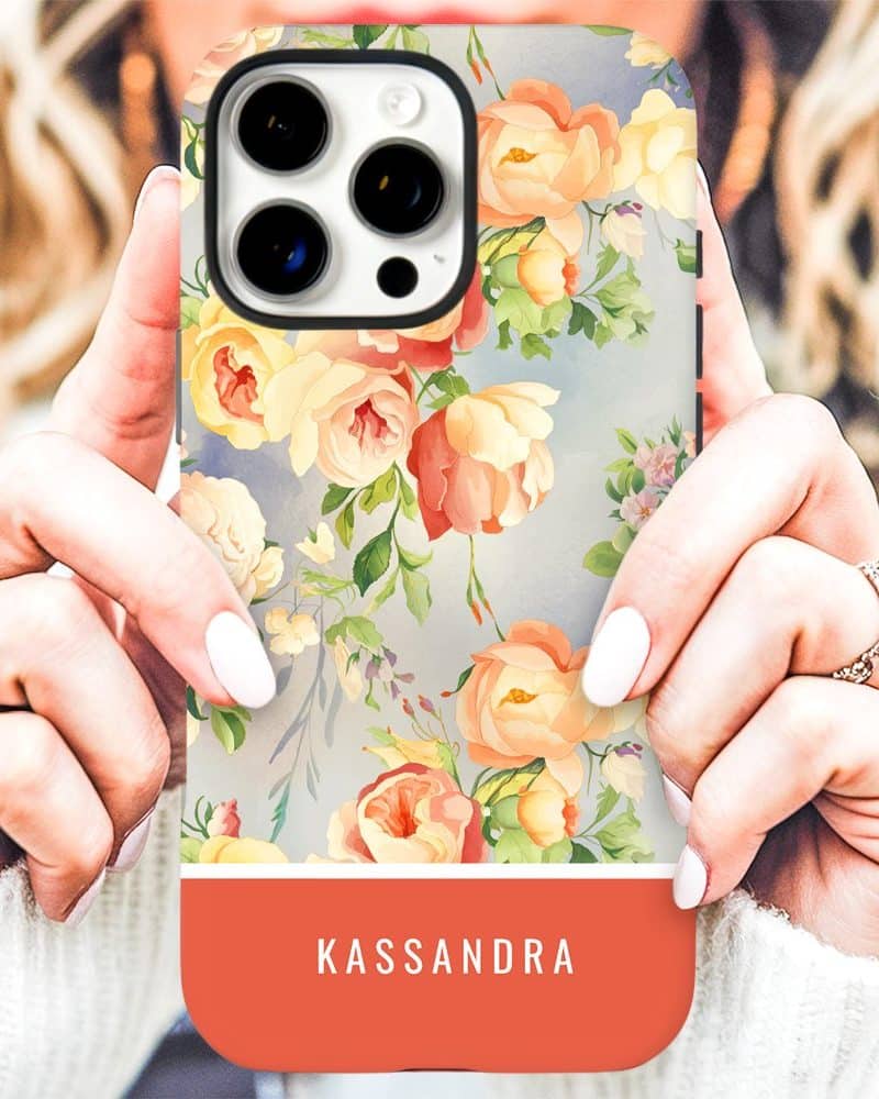 A woman's hands holding a phone case with a floral design and the name Kassandra on a coral band.