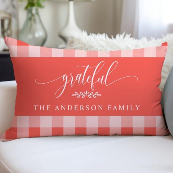 Coral Rectangular Pillow With A White Gingham Border And The Words Grateful, The Anderson Family In A White Script Font.