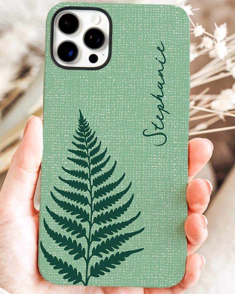 A hand holds a sage green phone case featuring a dark green fern and the name Stephanie.