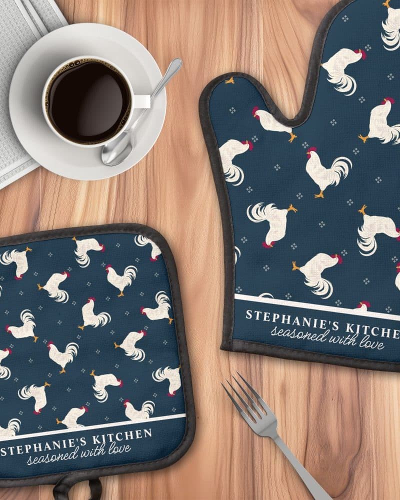 A dark blue oven mitt and pot holder with a white rooster pattern and personalized text.