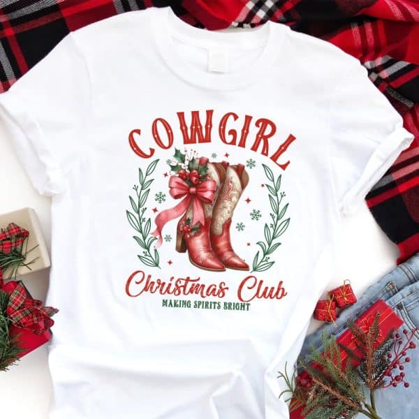 White T-Shirt With Red Cowgirl Boots, A Bow, And Holly Design; Text Reads Cowgirl Christmas Club, Making Spirits Bright.