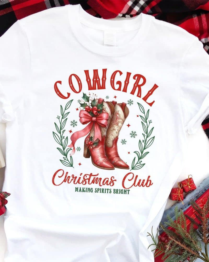 White t-shirt with red cowgirl boots, a bow, and holly design; text reads Cowgirl Christmas Club, Making Spirits Bright.