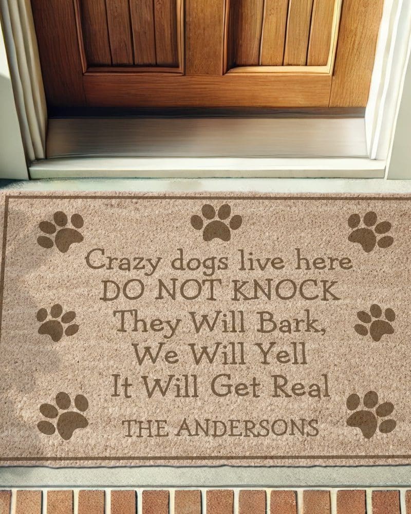 Tan doormat with the text Crazy dogs live here, DO NOT KNOCK, They Will Bark, We Will Yell, It Will Get Real, and The Andersons. Paw prints are also printed on the mat.