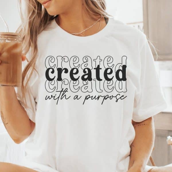 Woman Wearing A White T-Shirt With The Word Created Stacked Three Times And The Phrase With A Purpose Underneath.