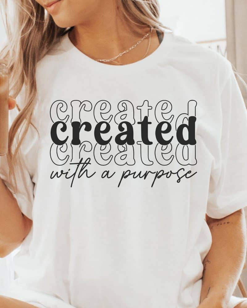 Woman wearing a white t-shirt with the word Created stacked three times and the phrase with a purpose underneath.