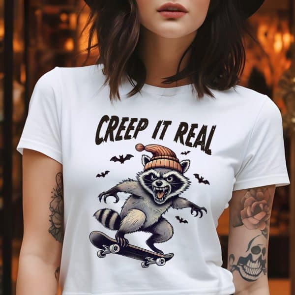 White T-Shirt Featuring A Graphic Of A Skateboarding Raccoon Wearing A Beanie. The Text Creep It Real Is Above The Image.