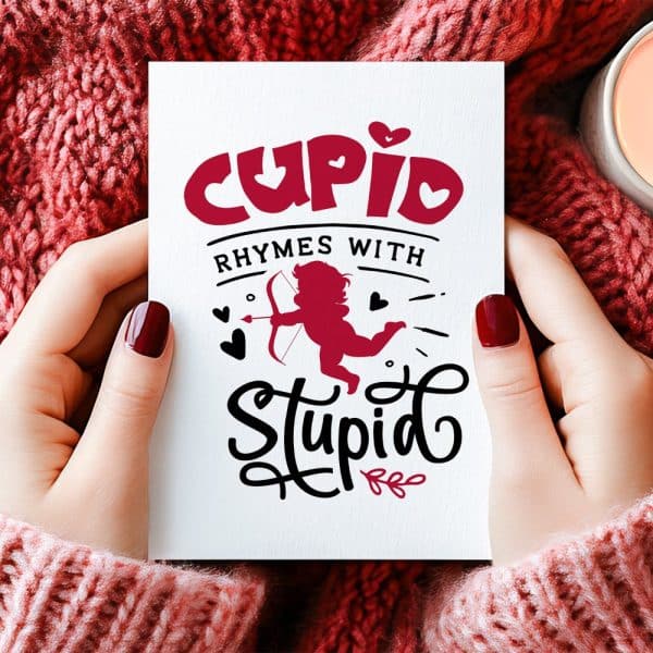 Two Hands Hold A Valentine'S Day Card Featuring A Cupid Silhouette And The Text Cupid Rhymes With Stupid.