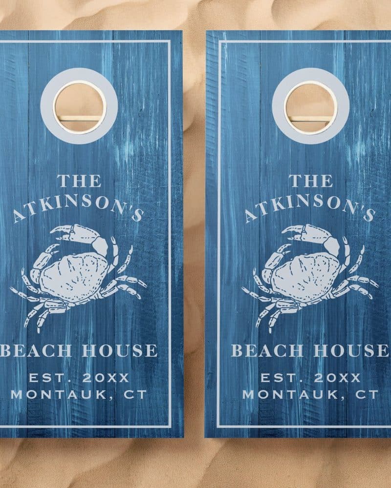 Pair of blue personalized cornhole boards, each featuring a crab illustration and beach house text.