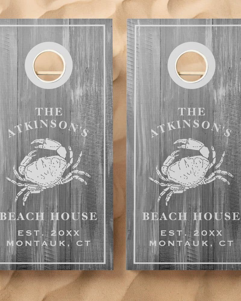 Pair of gray wooden cornhole boards with a crab design, The Atkinsons Beach House text, and establishment date.