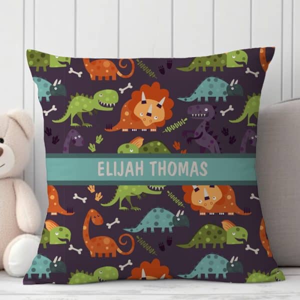 Personalized Square Pillow With A Repeating Pattern Of Colorful Cartoon Dinosaurs On A Dark Purple Background. The Name Elijah Thomas Is Printed Across The Center.