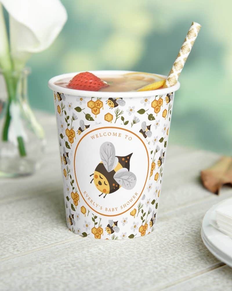 A paper cup with a bee-themed design for a baby shower, featuring a cartoon bee and the words "Welcome to Everly's Baby Shower".