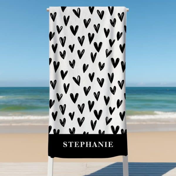A White Beach Towel With A Black Heart Pattern And The Name Stephanie At The Bottom.