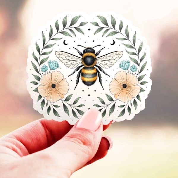 A Hand Holds A Circular Sticker Featuring A Bumble Bee Centered In A Floral Wreath.