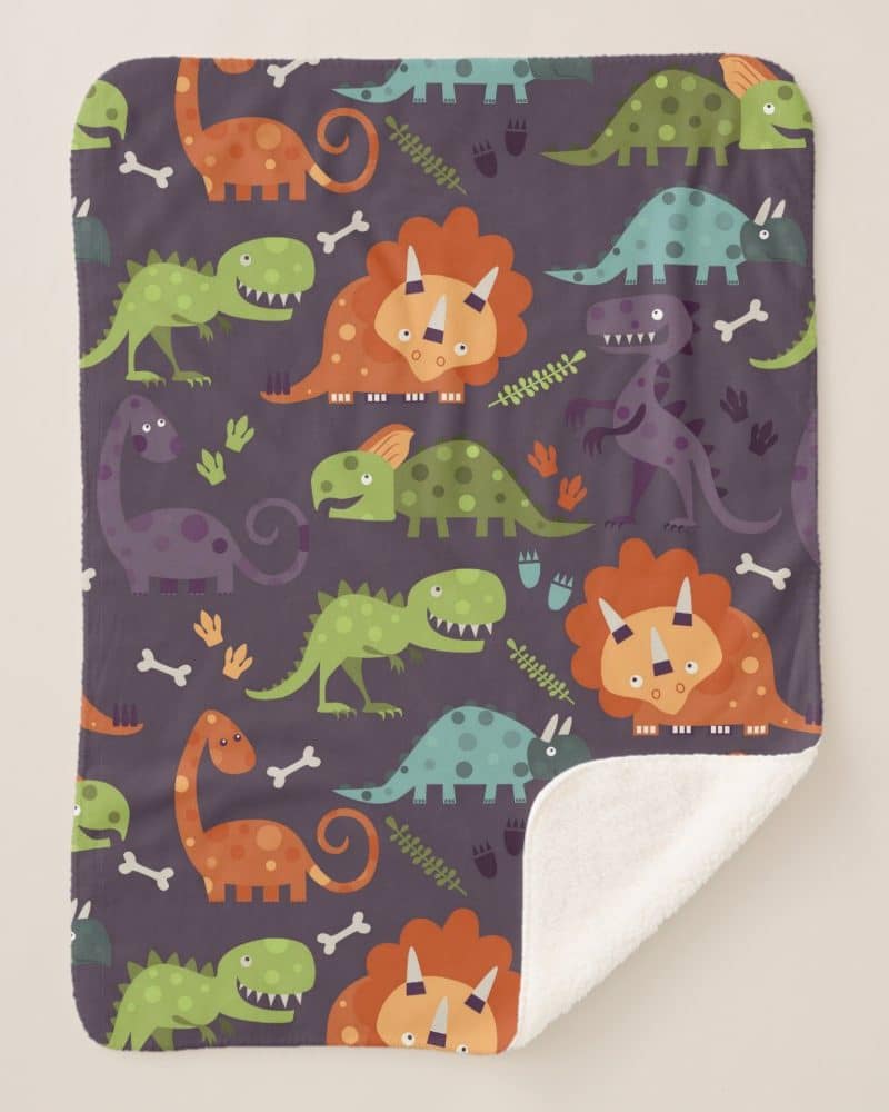 A fleece blanket with a repeating pattern of colorful cartoon dinosaurs on a purple background.